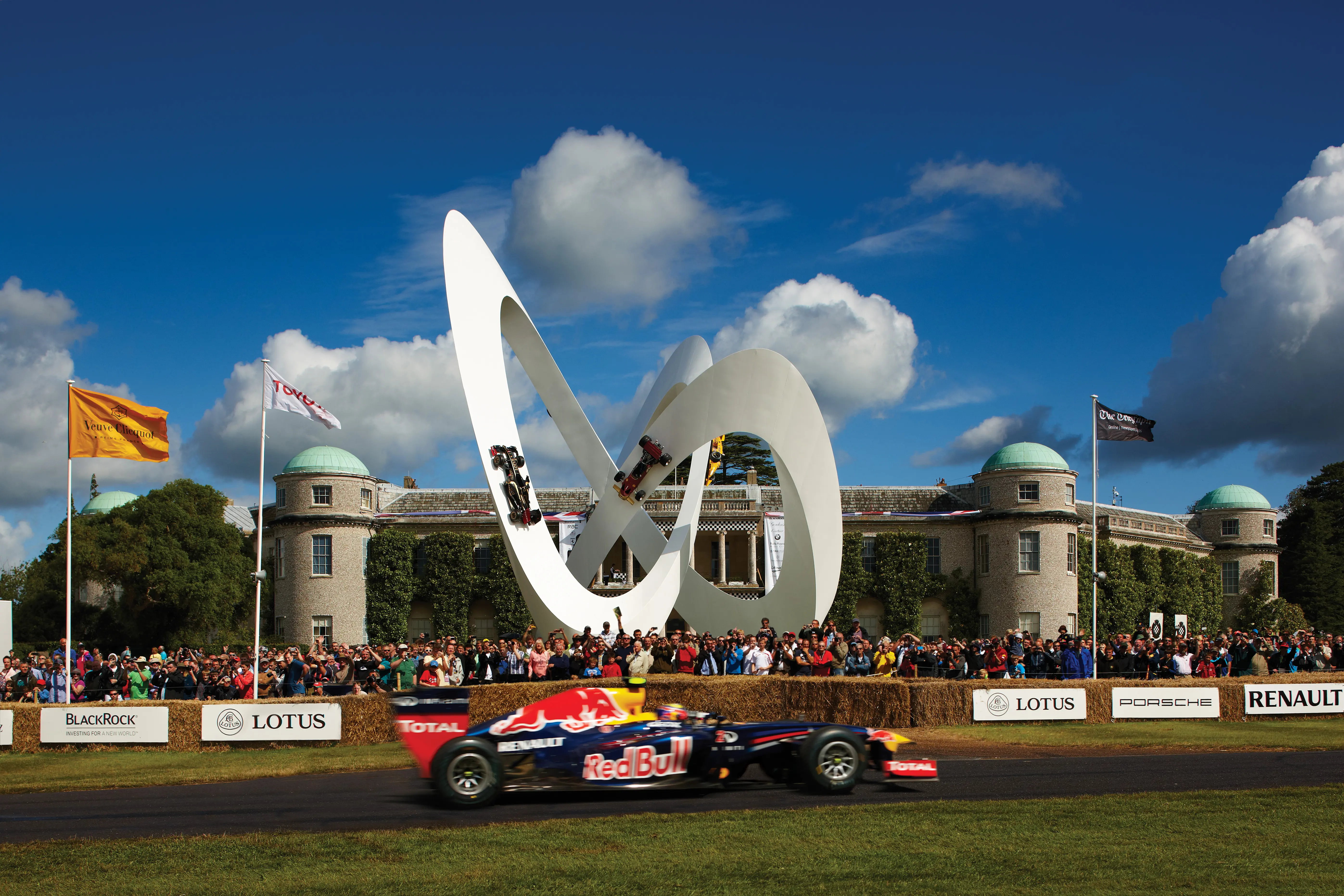 Racing car at the Goodwood Festival of Speed track with the big figure of eight sculpture created by Gerry Judah in the background.